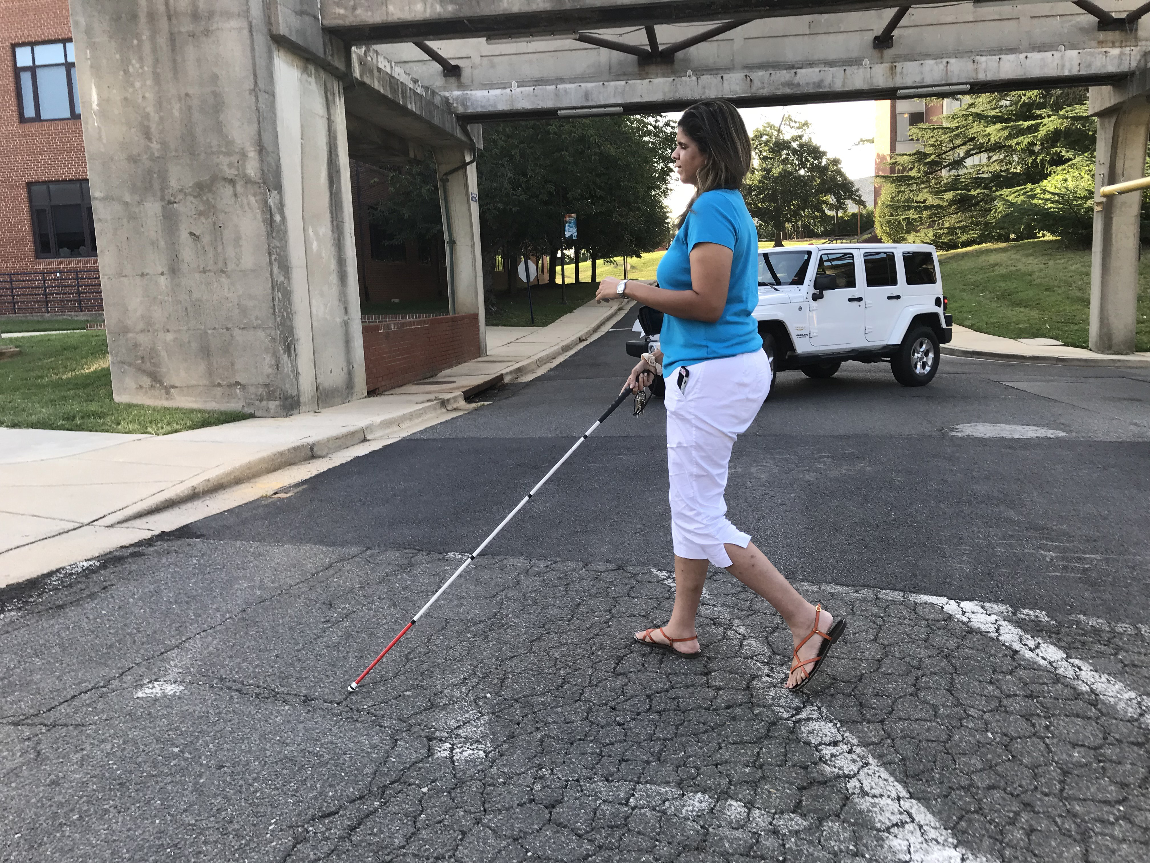 Three pictures show a student with a white cane, standing with one foot in the street.  A vehicle pulls out of the parking lot and waits while she crosses
